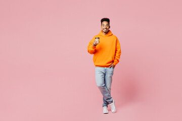 Full body young man of African American ethnicity wear yellow hoody casual clothes hold takeaway delivery craft paper brown cup coffee to go isolated on plain pastel pink background Lifestyle concept - Powered by Adobe
