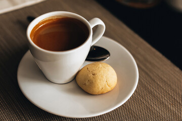 White cup of hot espresso coffee with a cookie on the table