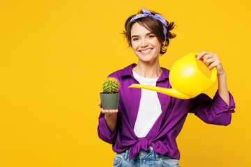 Young smiling happy cheerful woman she wear purple shirt rubber gloves casual clothes do housework tidy up water cactus plant isolated on plain yellow background studio portrait. Housekeeping concept. - obrazy, fototapety, plakaty