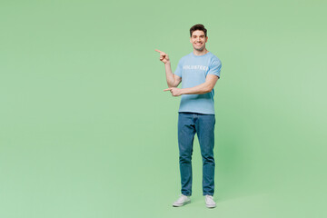 Full body smiling young man wears blue t-shirt title volunteer point index finger aside on area...
