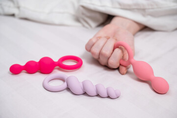 A woman chooses anal beads from a set while lying in bed. 