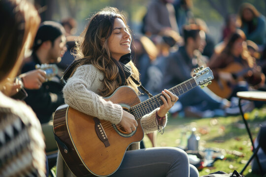 young woman playing guitar with friends attend a live music event concert in a park