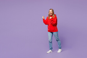 Full body side view young blonde woman wears red hoody casual clothes doing winner gesture...
