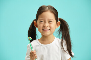 Cute Asian ethnicity child girl with a two ponytails holding toothbrush and happy smiling preparing...