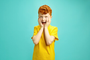 Delighted redheaded boy with a surprised expression standing over blue isolated