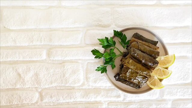 Delicious oriental dolma made of grape leaves stuffed with rice, with parsley and lemon, on a ceramic plate