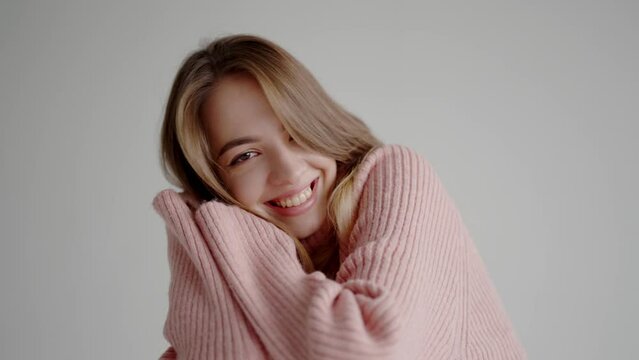 Young beautiful woman in pink knitted sweater smile and looking at camera in studio with white background. Portrait of cheerful pretty female