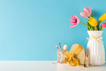 Commemorating 8 March and Mother's Day with side view tableau of womanly items: fine jewelry, beauty brushes, lip color, giftbox and fresh tulips, arranged on table, light blue wall behind, text space
