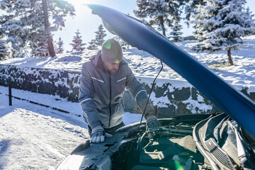 Man looking under the car hood of broken vehicle on snowy road and checking the problem.