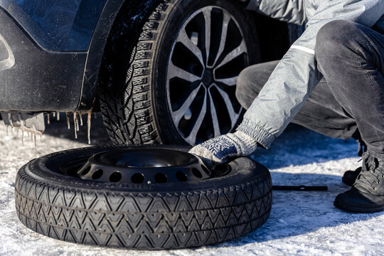 Close up of man replacing flat tyre with spare wheel on snowy road.