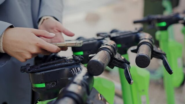A video capturing a person holding a cell phone in front of a line of green bicycles. Person Holding Cell Phone in Front of Row of Green Bicycles