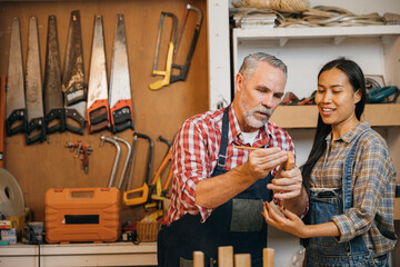 Craftsmen senior man teaching woman apprentice at woodshop, Carpenter training wood for female...