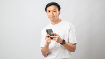 Portrait of an Indonesian Asian man, wearing a white T-shirt, looking expressive at his smartphone, isolated against a white background.