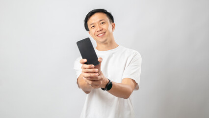 Fototapeta premium Portrait of an Indonesian Asian man, wearing a white T-shirt, showing the blank screen of his smartphone, isolated against a white background.