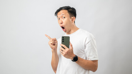 Portrait of an Indonesian Asian man, wearing a white T-shirt, holding a smartphone and pointing in a specific direction, isolated against a white background.