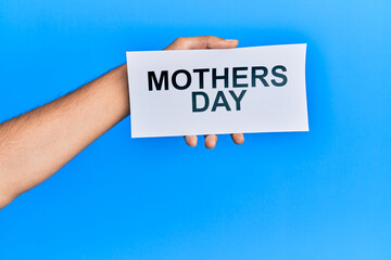 Hand of caucasian man holding paper with mothers day message over isolated blue background