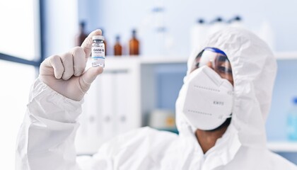 Young hispanic man scientist wearing medical mask holding covid vaccine dose at laboratory