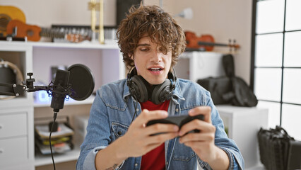 Engrossed young man with headphones using smartphone in a home music studio.