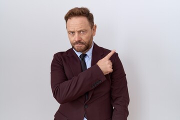 Middle age business man with beard wearing suit and tie pointing with hand finger to the side showing advertisement, serious and calm face