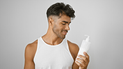 Handsome young hispanic man examining a skincare product against a white background, conveying a sense of grooming and wellbeing.