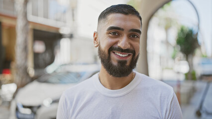 Handsome bearded man smiling outdoors in a city, depicting urban lifestyle and positivity.
