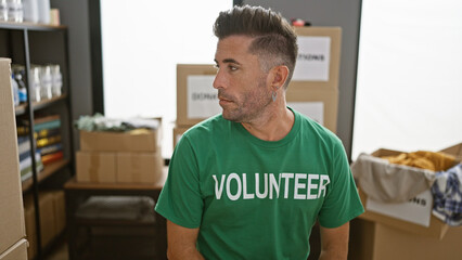 Handsome young hispanic man, concentrated on volunteering work at charity center, sitting at table, with serious face. portrait of community service adult, looking to the side indoors.