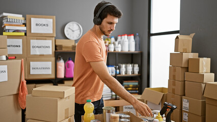 A young hispanic man with a beard organizing donations in a warehouse while wearing headphones.