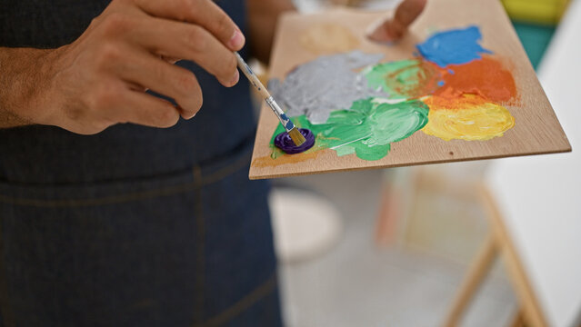 Close-up of a man's hand mixing paint colors on a palette in an indoor art studio setting.