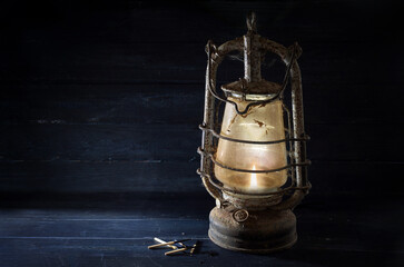Rusty kerosene lantern shines undaunted with light in the dark, obsolete technology in times of...