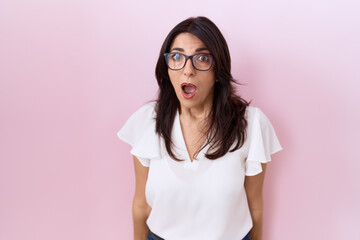 Middle age hispanic woman wearing casual white t shirt and glasses afraid and shocked with surprise...