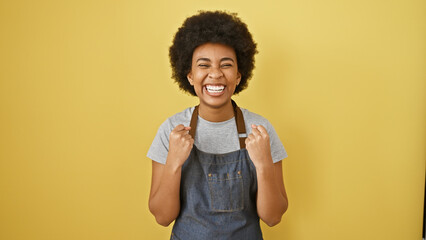 Joyful african american woman with curly hair laughing in front of a yellow background, wearing a...