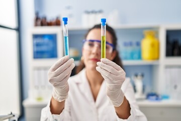 Young beautiful hispanic woman scientist holding test tubes at laboratory