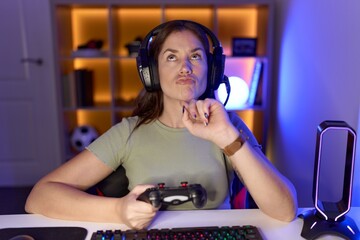 Beautiful brunette woman playing video games wearing headphones thinking concentrated about doubt...