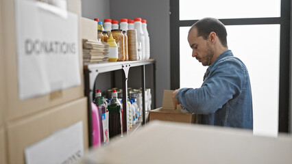 Hispanic man organizing donations in a warehouse with shelves of food and supplies in the background