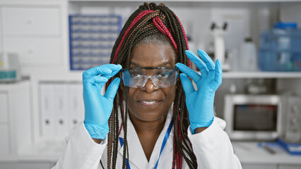Focused adult african american woman scientist with glasses and serious expression, immersed in...