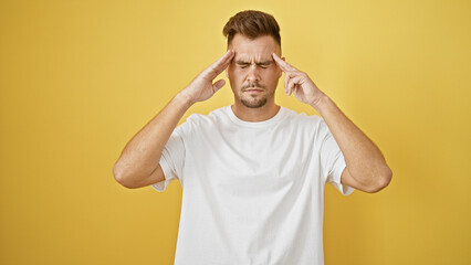 A young hispanic man with a beard poses against a yellow background, exhibiting stress or headache...
