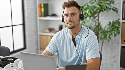 A young hispanic man with a beard in a blue shirt using a headset in a modern office room.