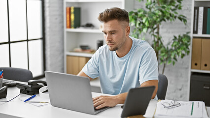 Handsome hispanic man working on laptop in a modern office setting.