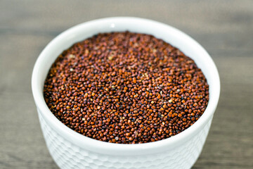 Red quinoa on the white plate on the wooden background. Healthy food and nutrition concept. Safe, ecological, and healthy products