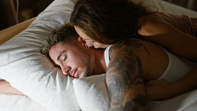 Intimate moment of a tattooed couple embracing while resting in a bedroom, depicting love and comfort.
