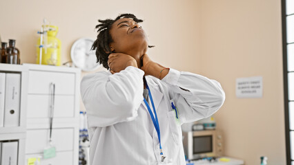 A young african american woman with dreadlocks wearing a lab coat appears stressed in a clinical...