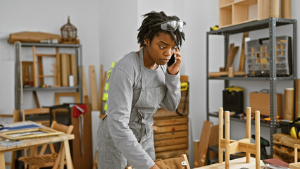 African woman with dreadlocks talking on the phone in a workshop setting indicates a busy woodwork...