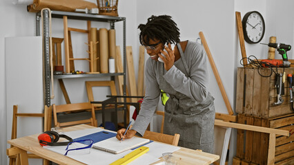 A young woman with dreadlocks talks on the phone while taking notes in a carpentry workshop