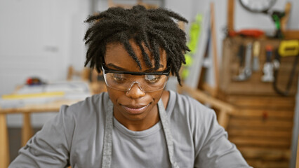 A focused young woman with dreadlocks wearing safety glasses in a woodworking workshop