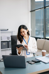 Confident business expert attractive smiling young woman typing laptop and holding digital tablet on desk in office.