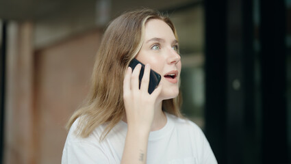 Young caucasian woman talking on smartphone with surprise expression at street