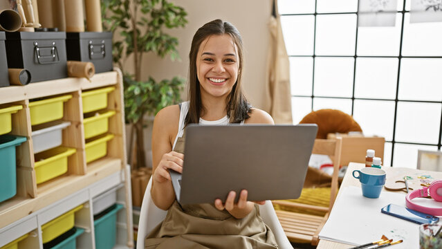 Young beautiful hispanic woman artist smiling confident using laptop at art studio