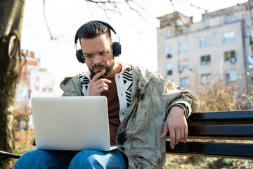 Young hipster millennial man world traveler nomadic living lifestyle sitting outdoor using laptop...