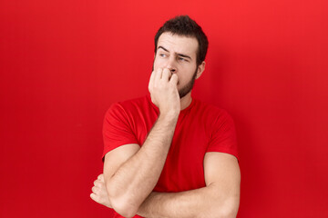 Young hispanic man wearing casual red t shirt looking stressed and nervous with hands on mouth...