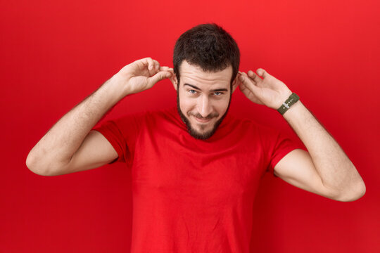 Young hispanic man wearing casual red t shirt smiling pulling ears with fingers, funny gesture. audition problem